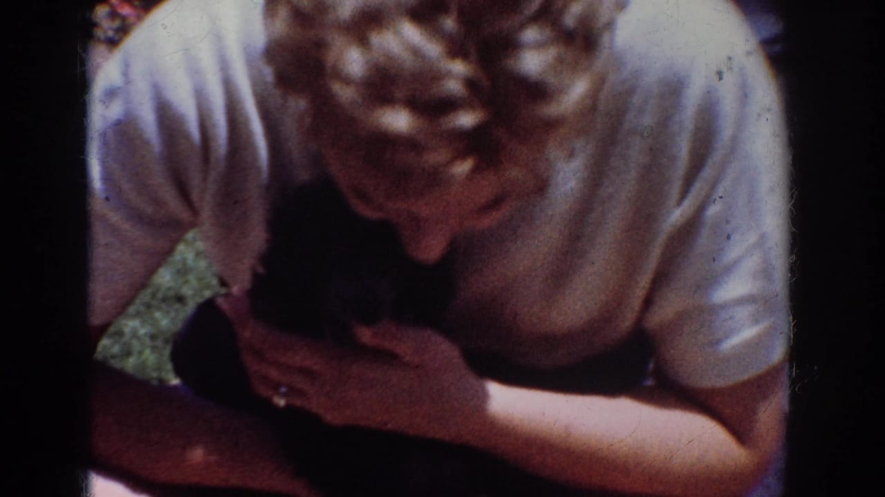 Woman in a light shirt bends over and holds a small black puppy.