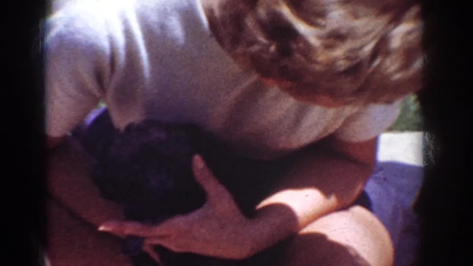 In the Yorba Linda 8mm footage, the woman cradles the small black puppy against her lap in bright outdoor light.