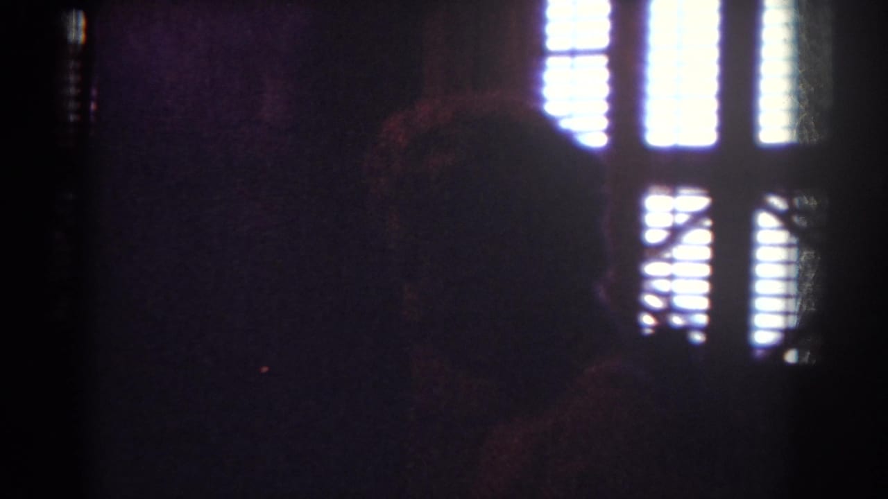 Dark 8mm interior frame with a silhouetted figure or shape near bright window blinds, likely from the same Yorba Linda home-movie sequence.