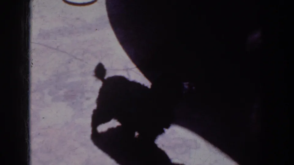 The dog’s dark profile shifts near a large rounded shadow across the light floor in this 1962 Yorba Linda 8mm frame.