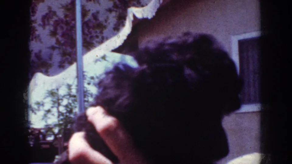 1962 Yorba Linda home-movie frame showing the black poodle puppy leaning downward as a person holds it near a window.