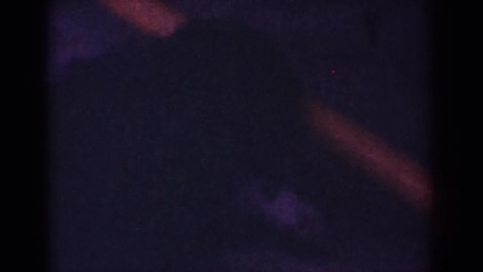 Low-light 8mm frame from the Yorba Linda clip showing shadowy purple tones, red-orange streaks, and no clearly identifiable subject.