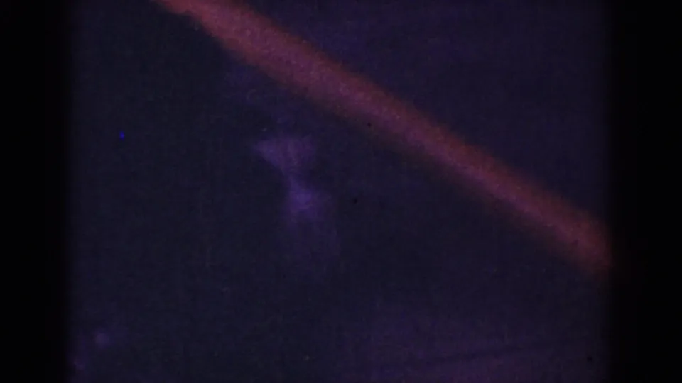 Underexposed 1962 home-movie frame with a diagonal reddish band, purple-black shadows, and indistinct motion in the darkness.