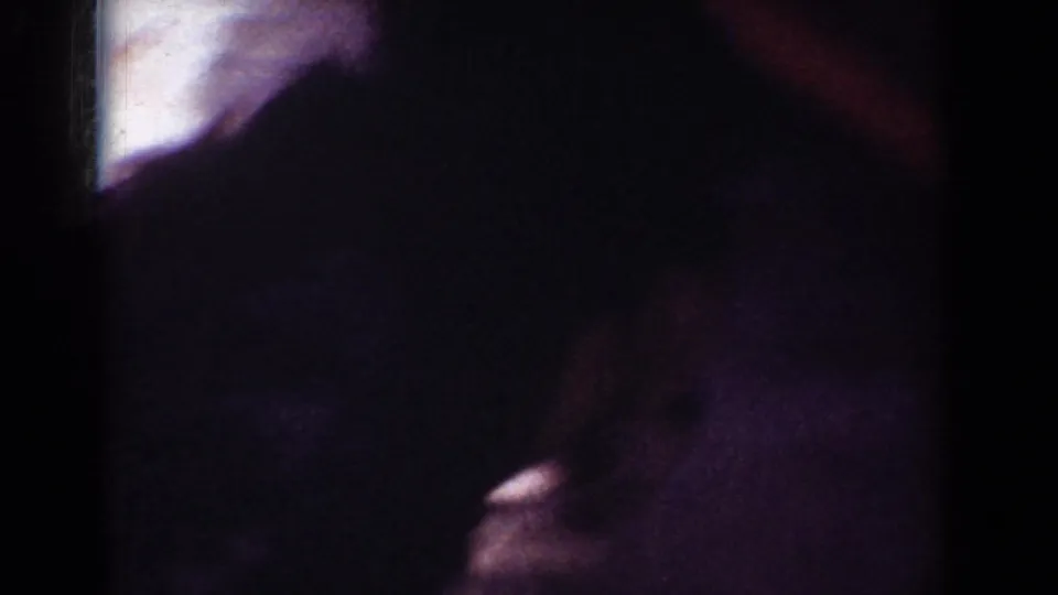 Underexposed 1962 Yorba Linda home-movie frame with a partial adult figure and a dog shape near the patio area.