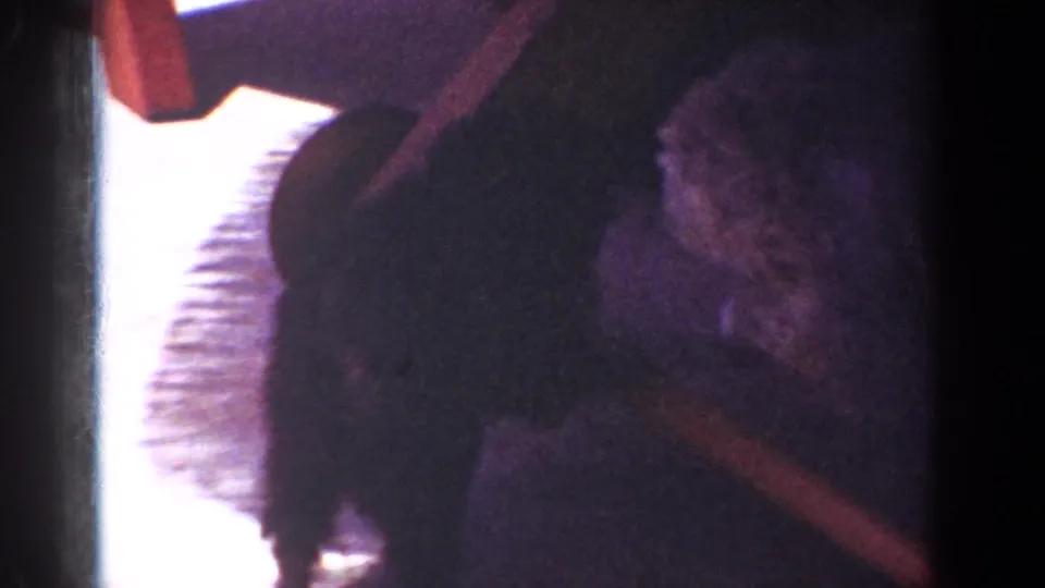 Yorba Linda 1962 home-movie frame showing a small dog on the patio near a person’s leg and a reddish tugging strap or toy.