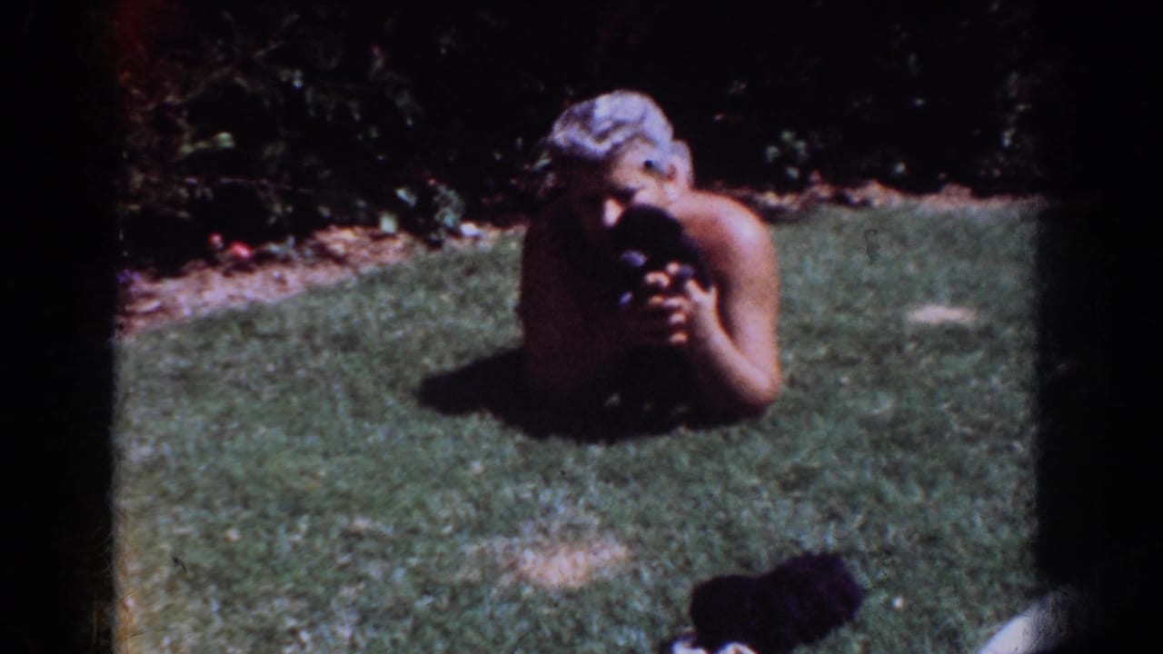 Gray-haired man lying on grass and cuddling a small black puppy.