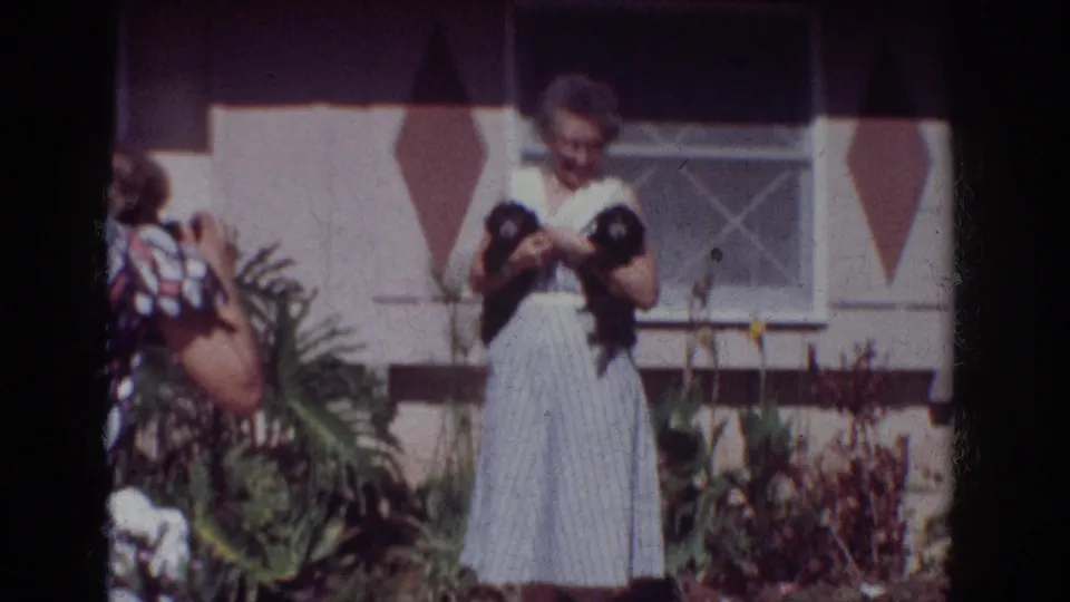 The final 1962 Yorba Linda frame shows the photographer at left and the woman holding two small black dogs in the residential garden.