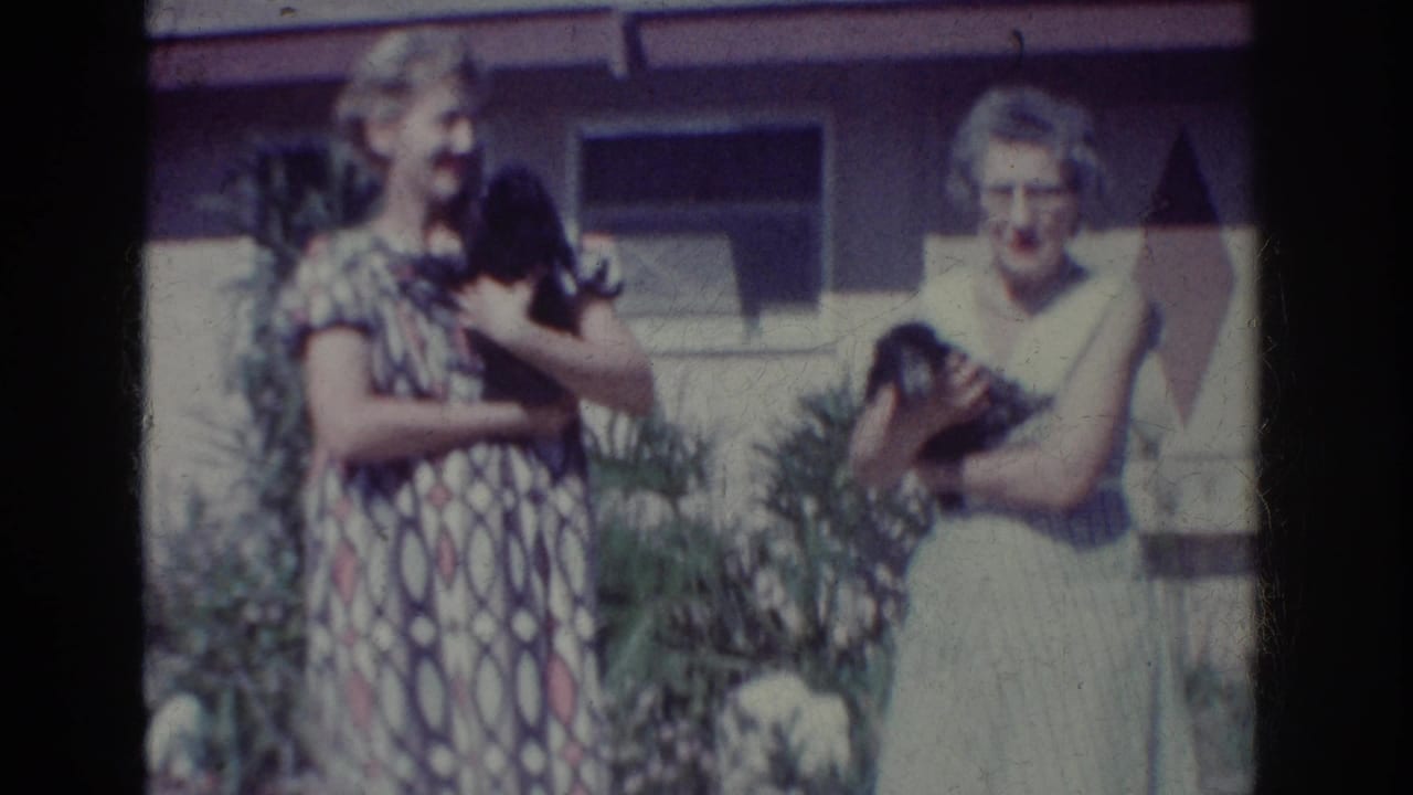 Two women stand outdoors holding small black puppies in front of a house.