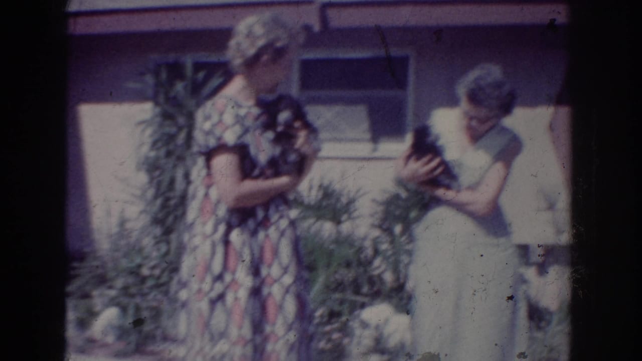 In Yorba Linda, California in 1962, two women hold small puppies in a front yard beside shrubs and a house wall.