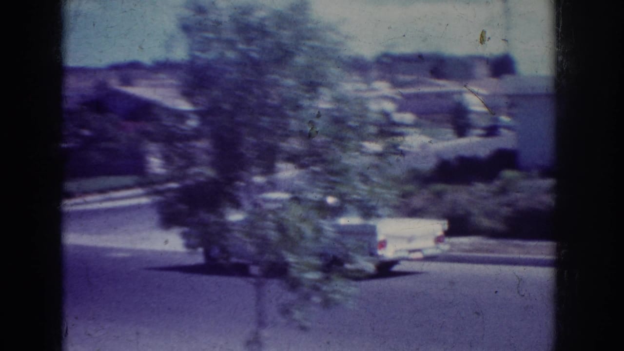 1962 Yorba Linda home-movie frame with a white car moving along a quiet residential street past trees and low houses.