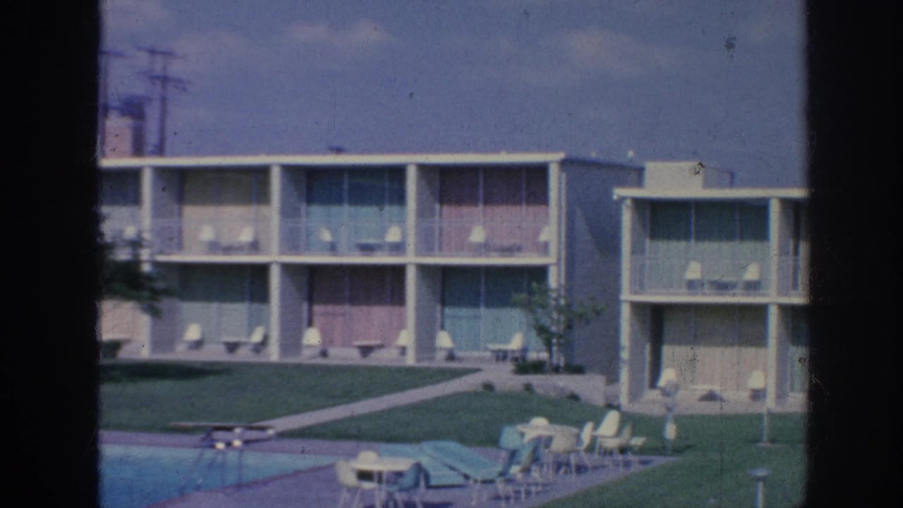 1963 Memphis motel pool view with balconies, colored panels, lawn, patio furniture, and guests near the water.