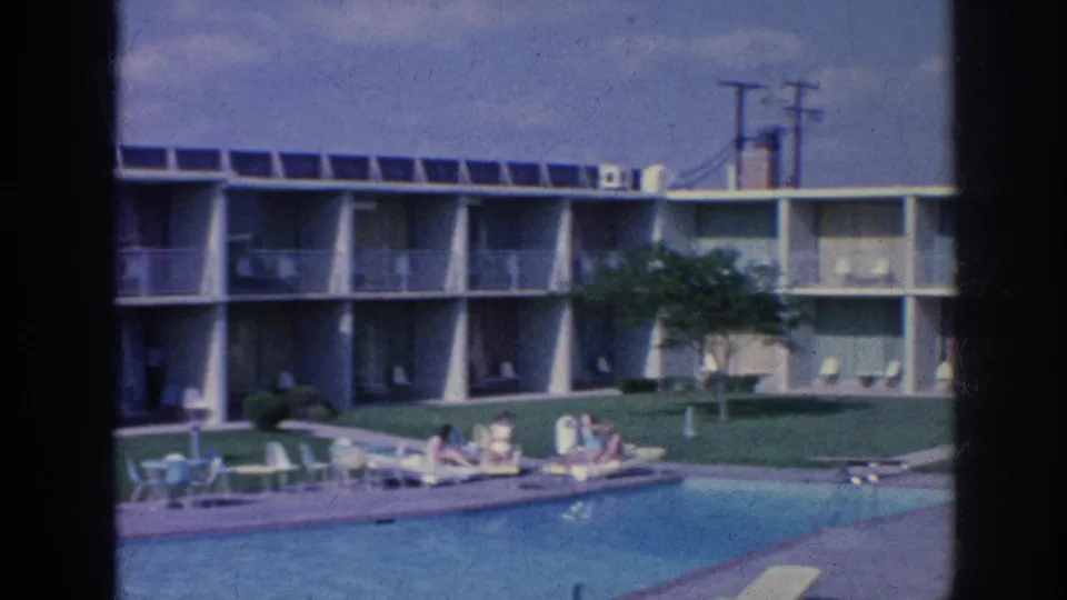 1963 motel pool scene in Memphis showing a two-story building, shaded balconies, lawn, chairs, and guests resting near the pool.