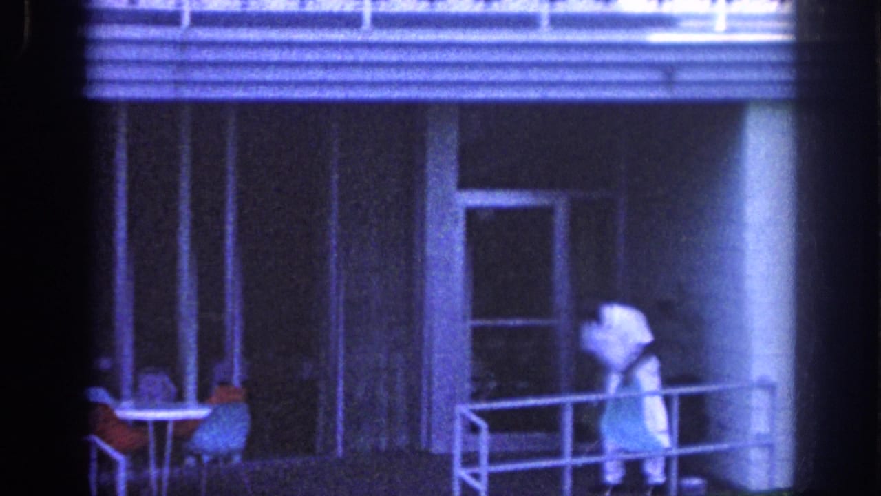 1963 Memphis 8mm frame showing a distant adult on a balcony, seen through dark vertical bars and blue-tinted film grain.