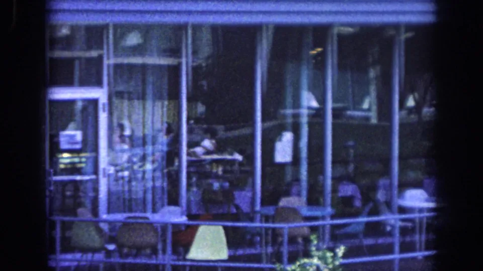 Blue 8mm frame from 1963 Memphis showing a balcony with glass doors, chairs, railing, and a distant adult in light clothing.