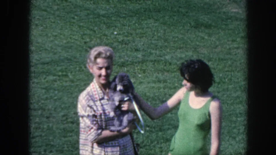 1963 Memphis 8mm frame showing two women on grass focused on a small dog held in front of the camera.