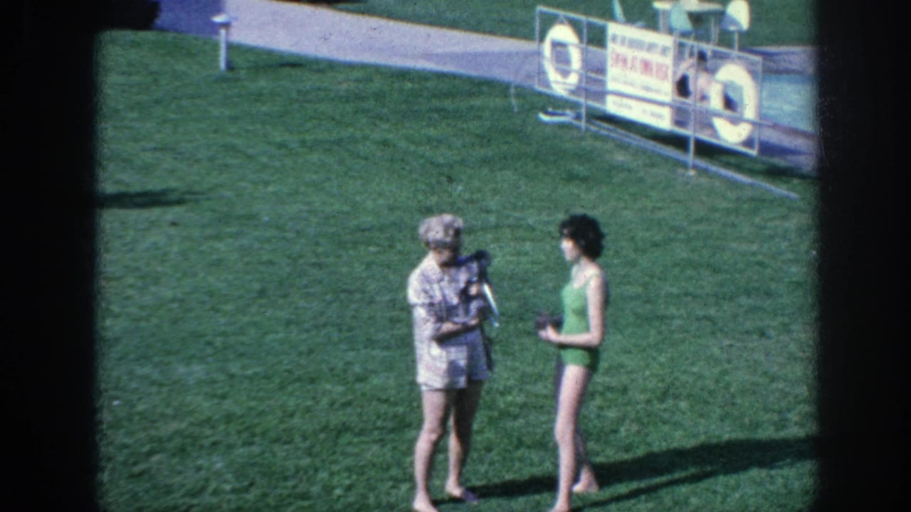 1963 Memphis-area 8mm frame showing two women on a poolside lawn, one holding a small dark poodle while speaking with a woman in a green swimsuit.