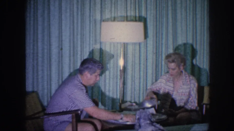 1963 Memphis frame showing the elderly man reaching toward the meal table as the woman looks down beside the lamp.