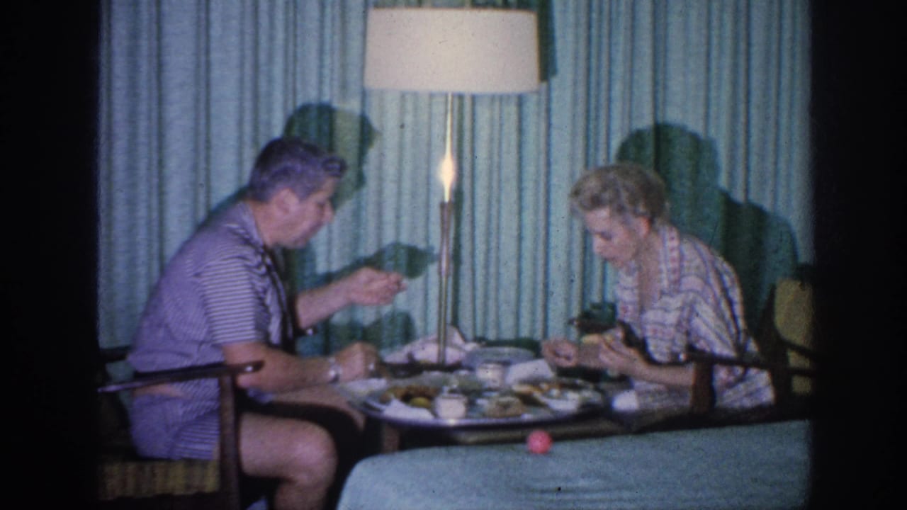 In 1963 Memphis home-movie footage, a man and woman sit at a small living-room table with dinner plates under a floor lamp.