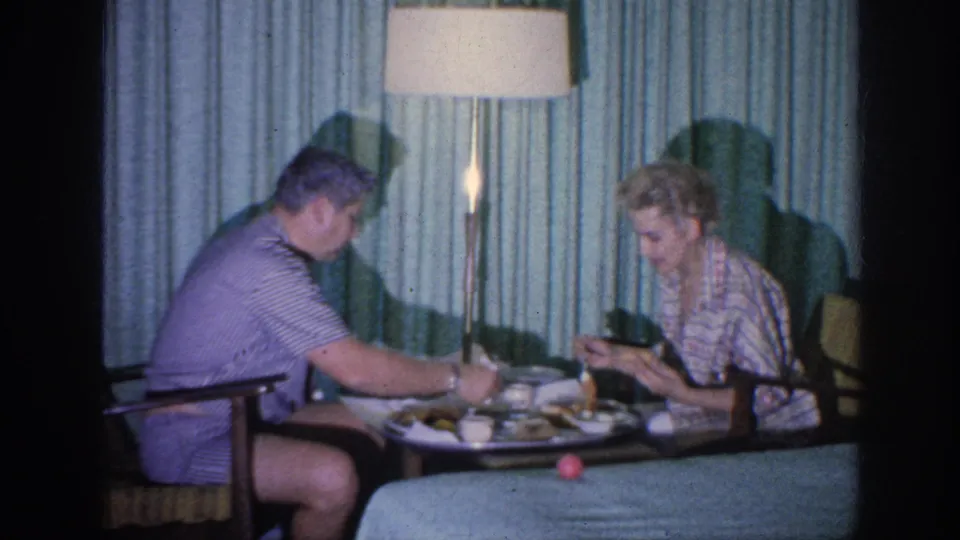 The couple remains seated at the meal table, with plates, cups, a floor lamp, and curtains visible in the 1963 Memphis interior.