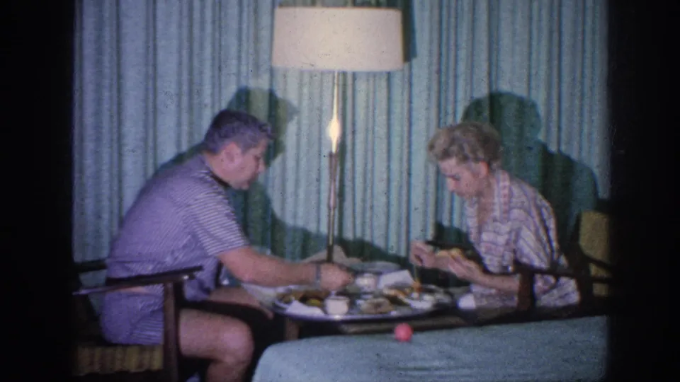 The woman looks down at a cup while the man sits across from her at the small table in a 1963 Memphis home interior.