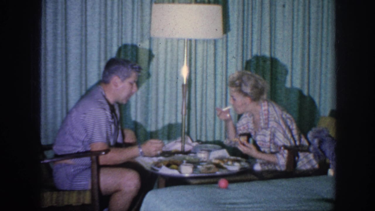 Man and woman sit at a small table eating from a tray in a hotel room.