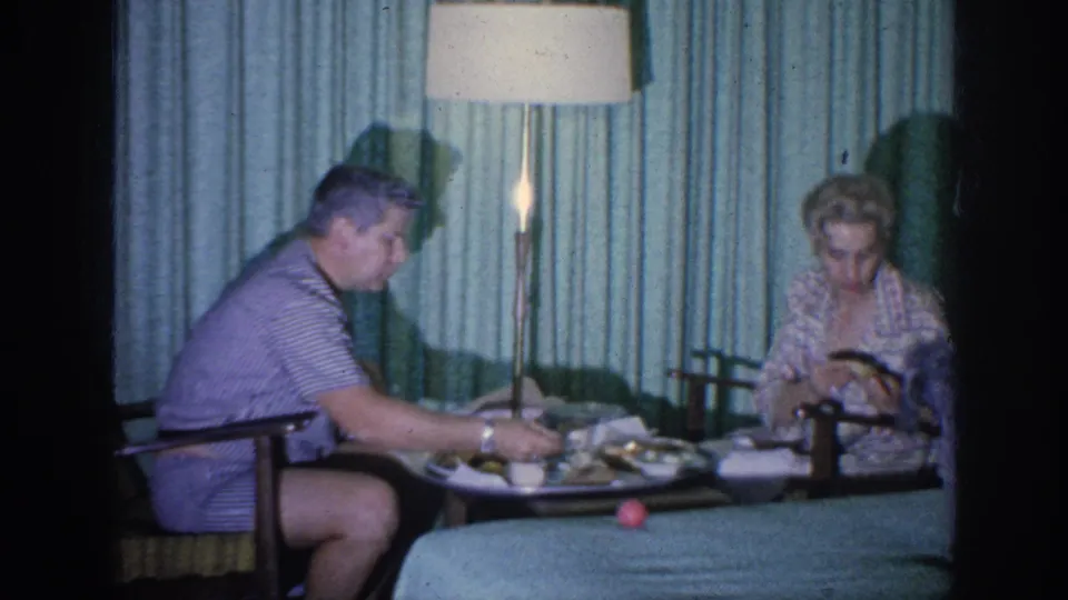 A 1963 hotel-room dining scene shows the man seated on the left and the woman looking down beside the meal tray.