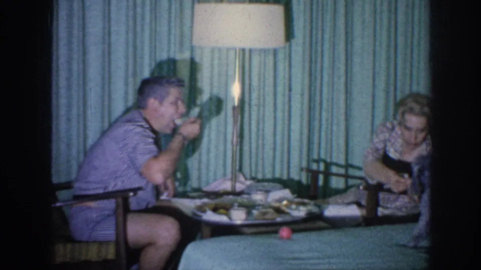 Near the end of the 1963 Memphis clip, the man eats while the woman leans toward the tray in the hotel-room interior.