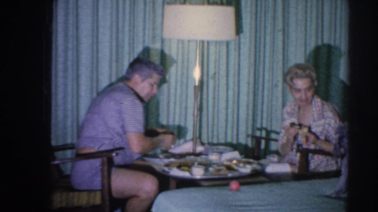 Couple continues eating at a small table beside a tall lamp and green curtains.