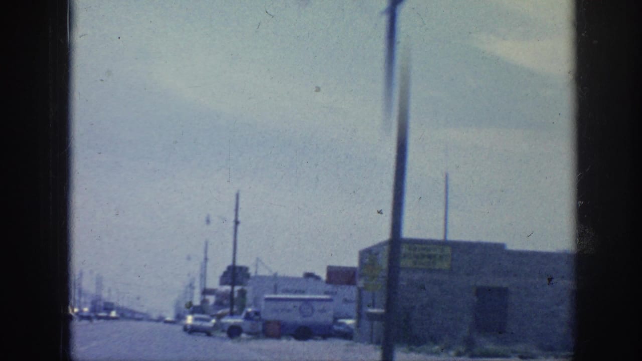 Industrial roadside with utility poles, low buildings, cars, and a commercial truck near the curb.