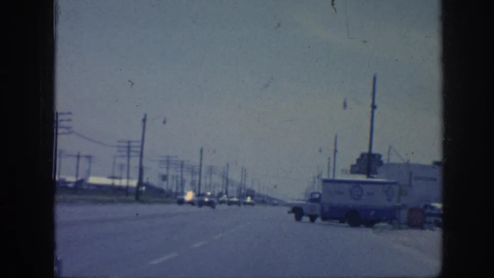 1963 Memphis roadway with utility poles, overhead wires, oncoming cars, and a commercial truck beside an industrial building.