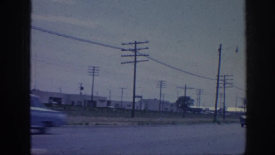 1963 Memphis industrial roadside with utility poles, overhead wires, low buildings, and a blurred car crossing the foreground.