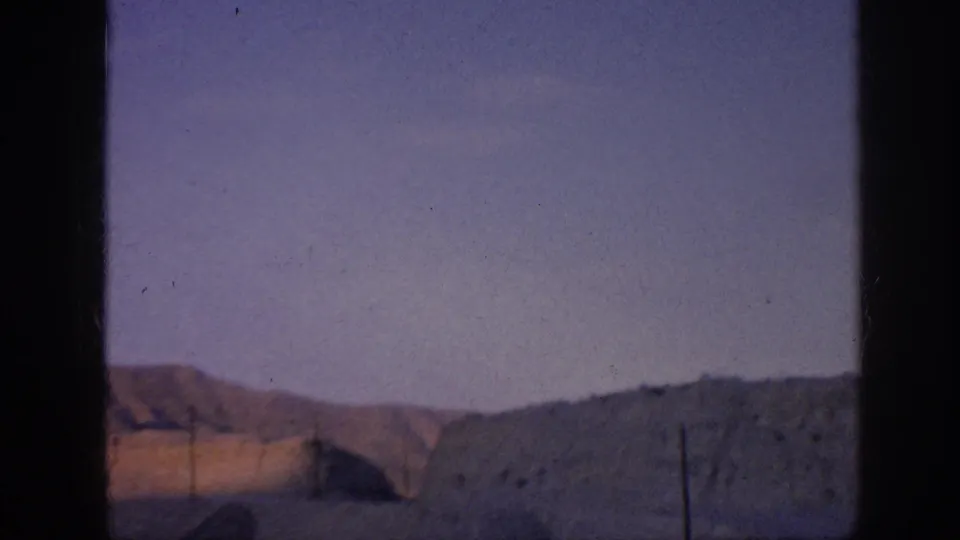 Distant rolling hills or mountains under a purple-blue sky, with a dark central border and visible 8mm film texture.