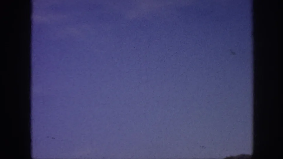 1963 8mm frame showing blue sky, faint cloud texture, and dark vertical film-frame edges.