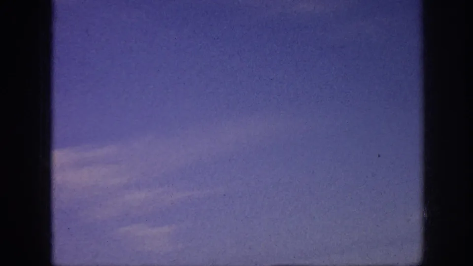 1963 8mm view of open blue sky with soft cloud streaks and heavy dark frame borders.