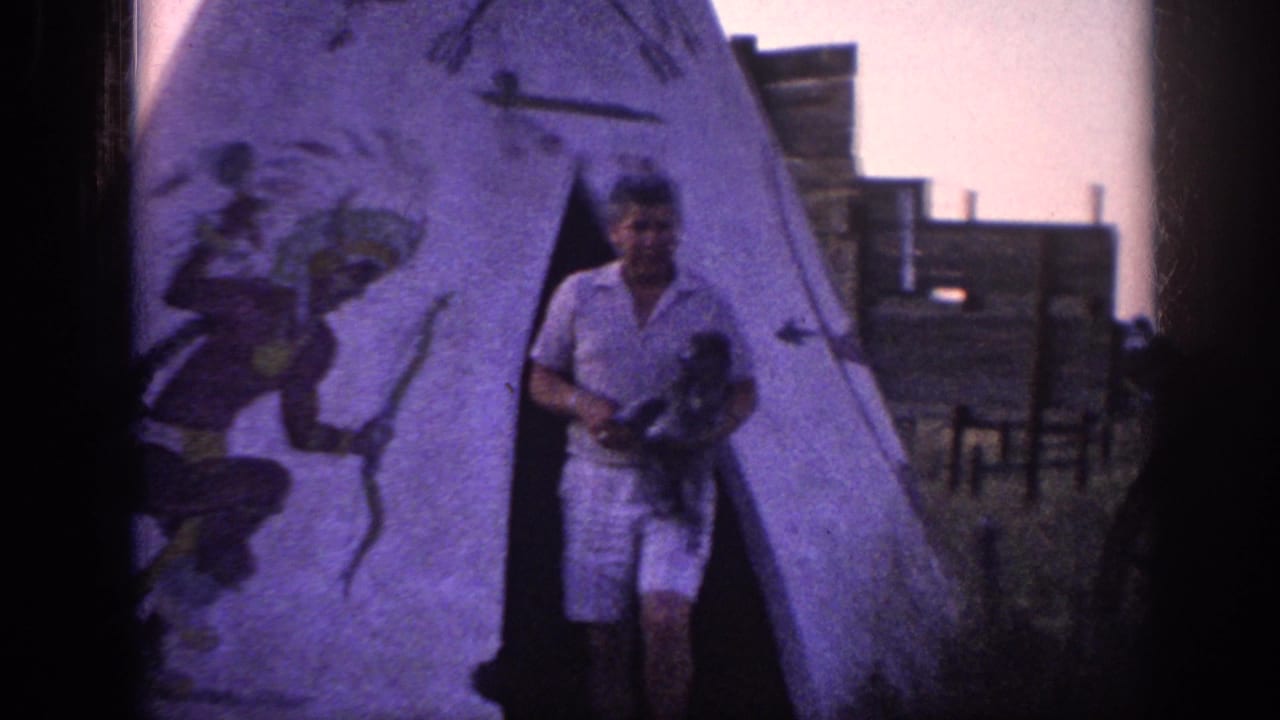 Man emerging from a painted teepee while holding a small dog.