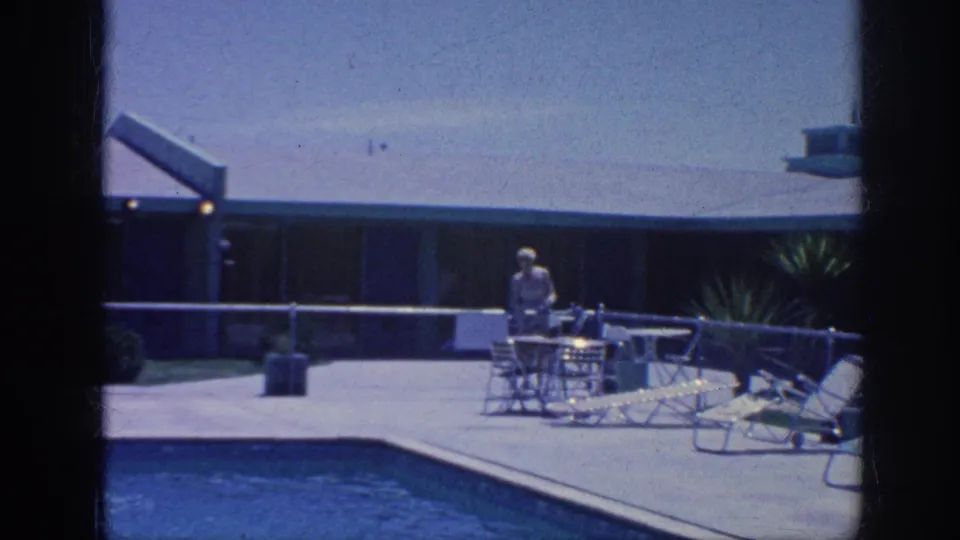 Wide 1963 Memphis home-movie view of a quiet pool deck with an adult near patio furniture and lounge chairs.