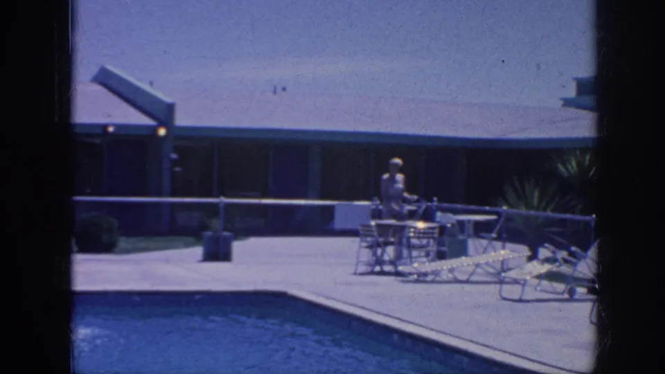 Blue-shifted 1963 Memphis vacation frame showing an adult on a sunny pool patio beside chairs and loungers.