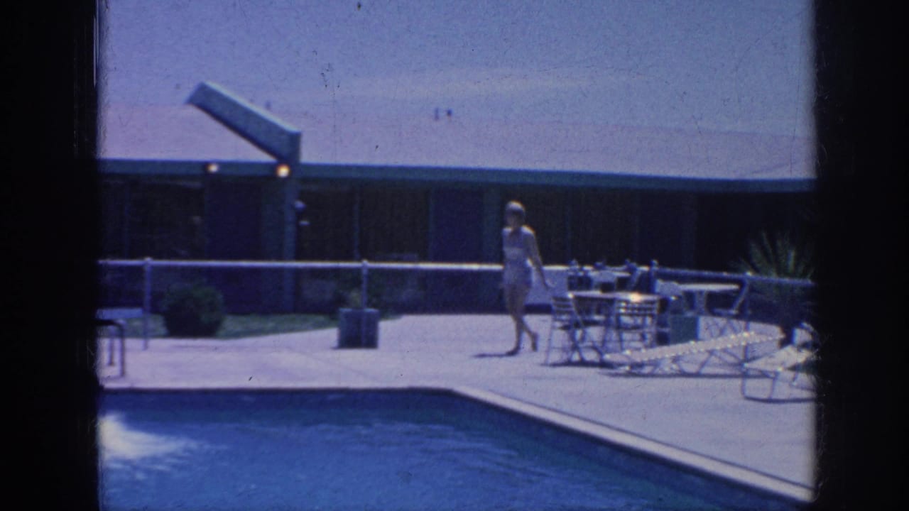Woman walking past patio furniture along the edge of a swimming pool.