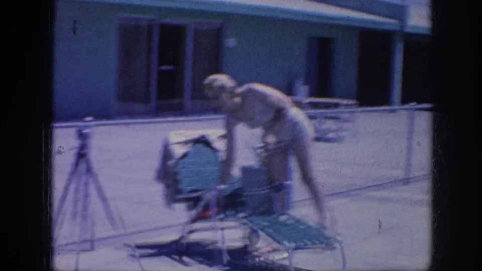 1963 Memphis poolside frame showing the woman bending over a green lounge chair to reach a purse or small bag.