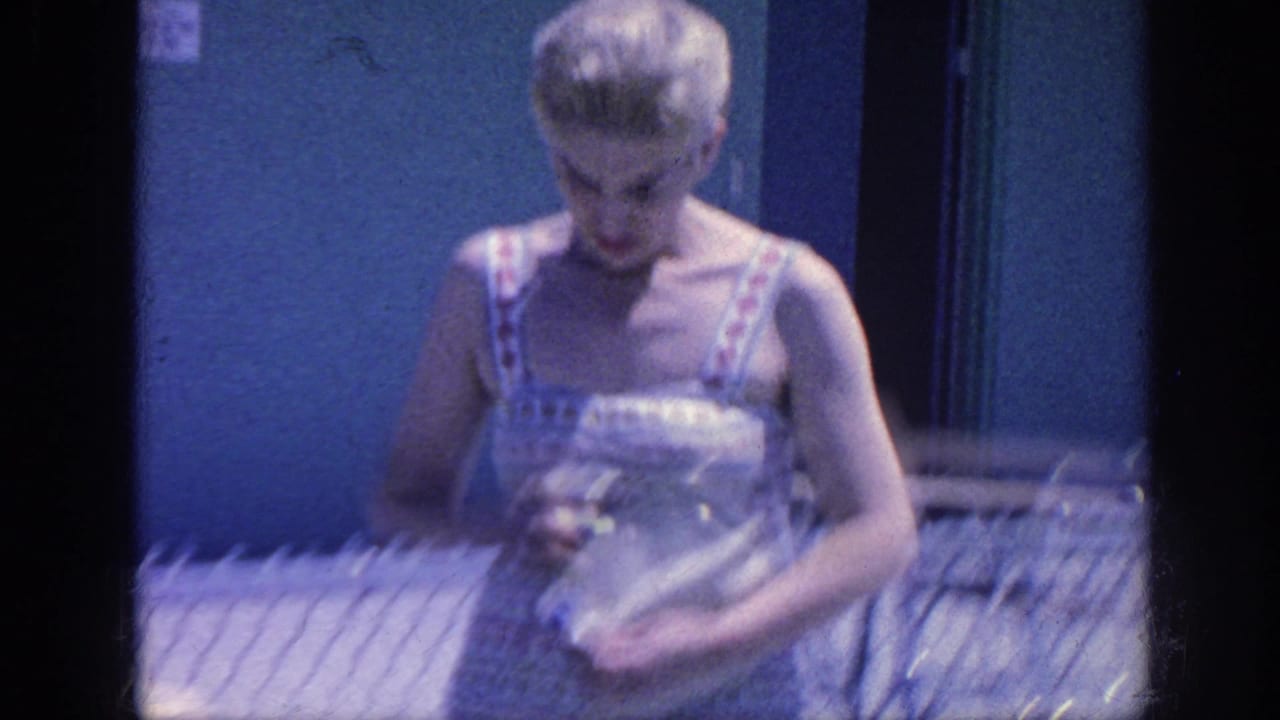 Adult woman in striped summer clothing looks down while standing near a pool fence.