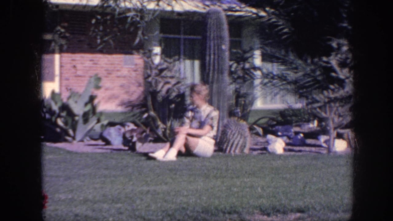 In 1963 Memphis home-movie footage, a woman sits on grass near cacti and garden rocks outside a brick house.