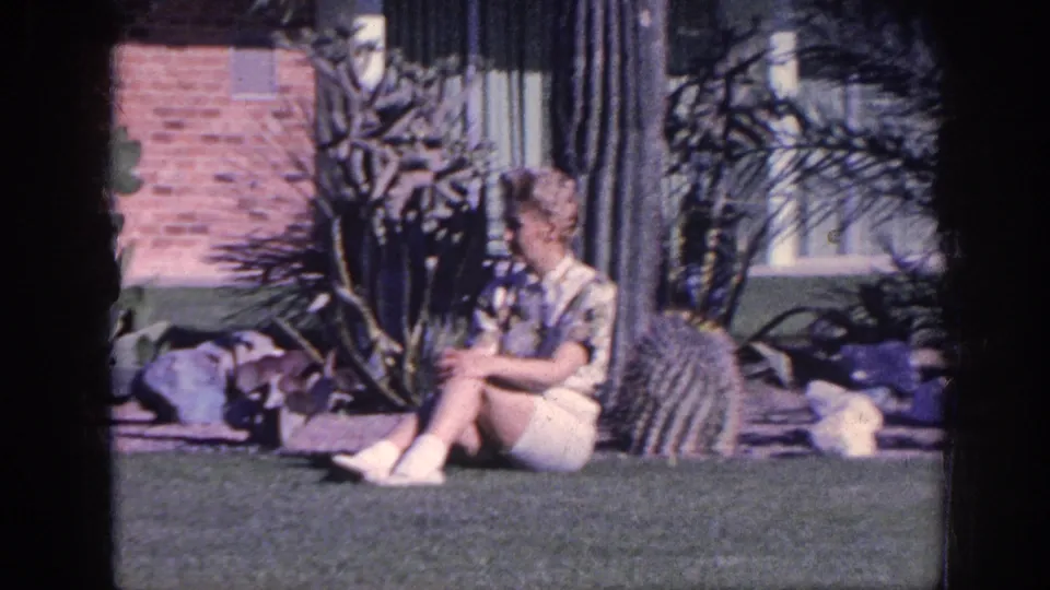 The woman remains seated in the Memphis garden, with a cactus, succulents, lawn and brick house behind her.