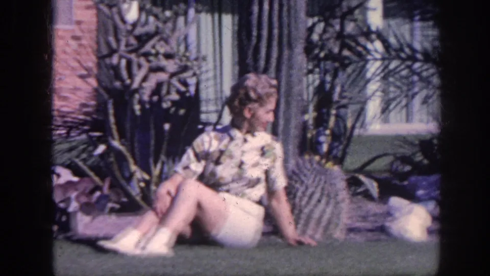 A closer 8mm frame shows the woman seated on the Memphis lawn, looking to the side beside cactus and garden stones.