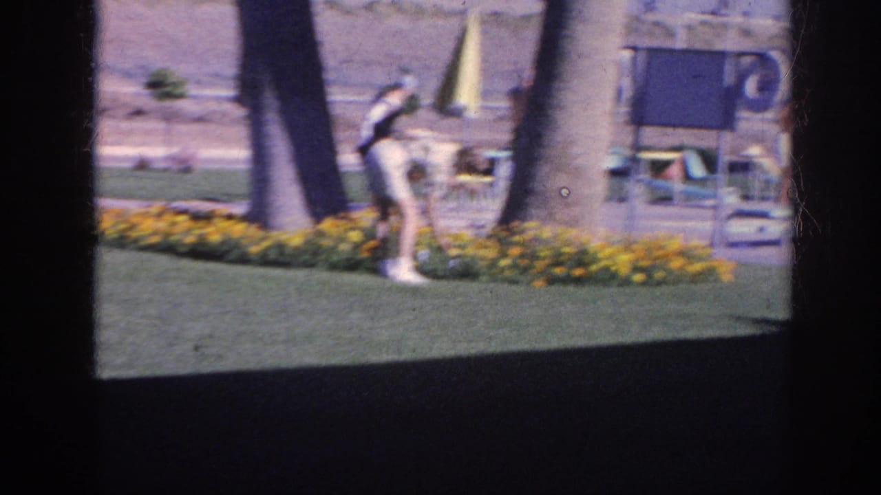 Woman bends near a flower bed while another adult stands farther back on the lawn.