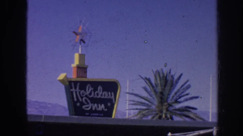 1963 Memphis home-movie frame showing a Holiday Inn sign and star logo against a clear sky, with a palm-like plant at the edge of the frame.