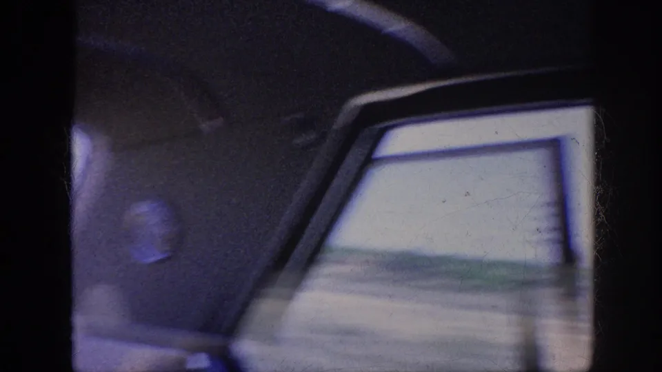 Inside a moving car in the supplied 1963 Memphis context, the rear side window frames a blurred road edge and low open land.