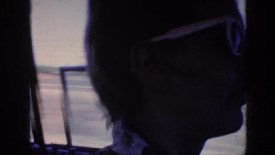 A woman in white-framed sunglasses appears in profile inside the car, with bright road and window light behind her.