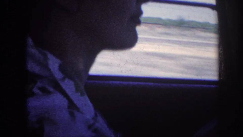 Close profile of a man in a 1960s car interior, flat open landscape visible through the side window, heavy blue cast on 8mm home-movie film, Memphis Tennessee 1963.