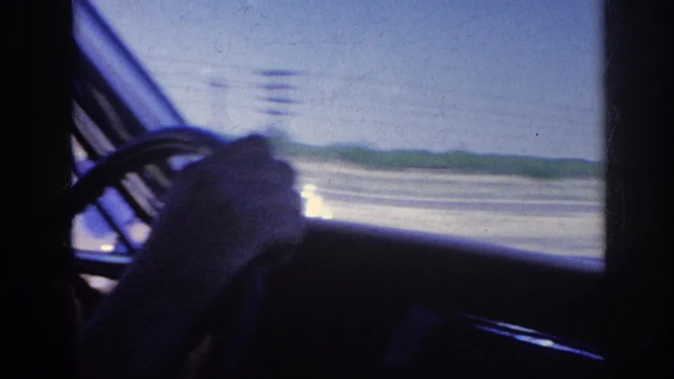 Open highway stretching to the horizon flanked by utility poles and a tree line, viewed through a car window, Memphis Tennessee area 1963, on 8mm home-movie film.
