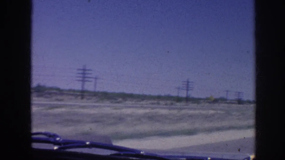 Final frame from the supplied 1963 Memphis-area driving clip showing an open road view through the windshield, utility poles along the roadside, and the car interior at the bottom edge.